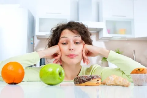 A woman contemplating healthy and unhealthy food choices on a kitchen counter.