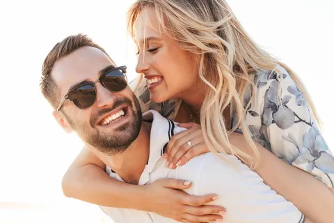 Happy couple enjoying a sunny day at the beach, smiling and embracing each other closely.