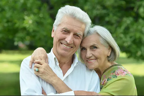 Smiling elderly couple embracing outdoors with greenery in the background on a sunny day