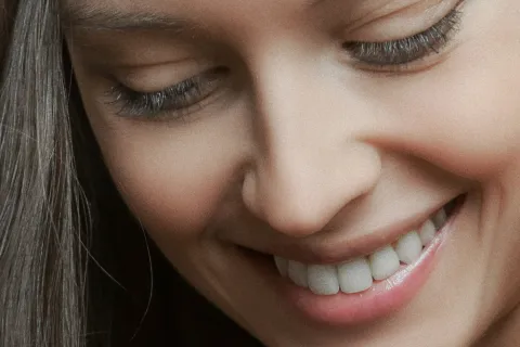 Close-up of a smiling woman with long dark hair and clear skin looking downwards.