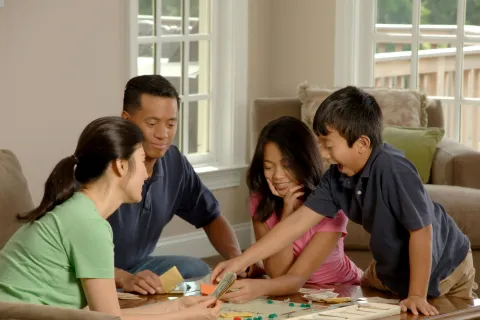 Family of four enjoying a board game together in a cozy living room with natural light.