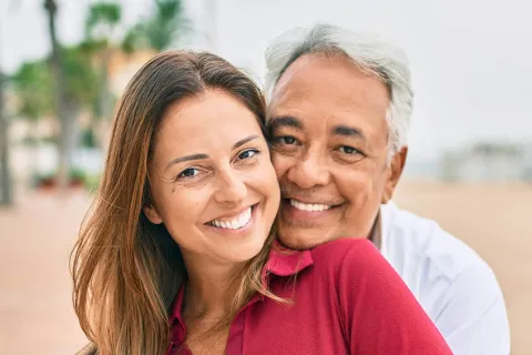Happy couple embracing outdoors, smiling at the camera, showcasing love and connection in a scenic setting.