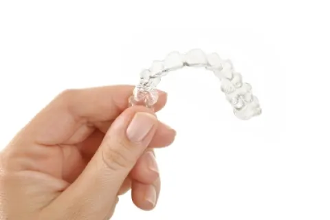 A hand holding a clear dental aligner for teeth straightening against a white background.