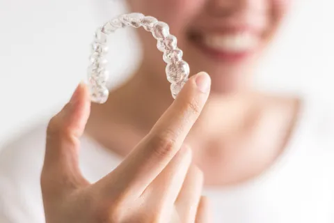 Person holding a clear dental aligner, showcasing its design and application.