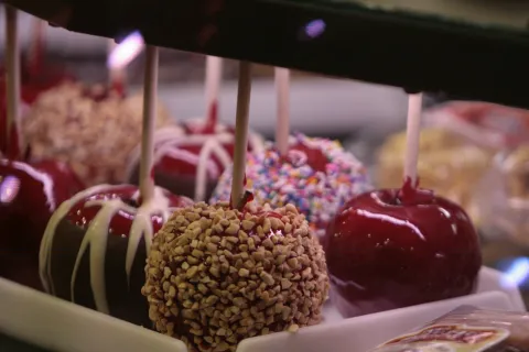 Variety of candy apples with nuts, sprinkles, and chocolate drizzle on sticks displayed in a case.