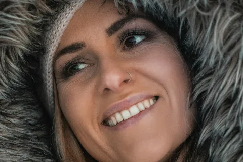 Smiling woman wearing a fur-lined hood and knit beanie in a close-up winter portrait.
