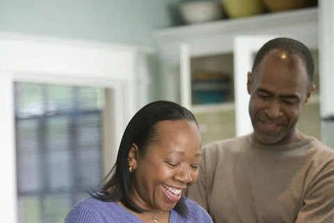Happy couple preparing vegetables together in a kitchen, peeling potatoes and smiling warmly.