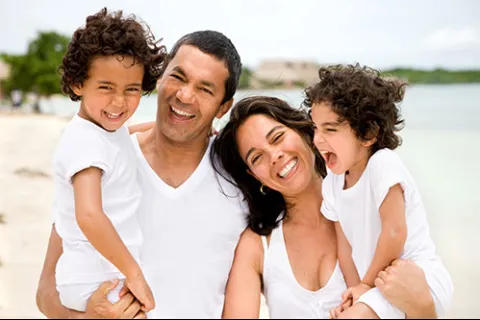 Happy family of four smiling and enjoying a beach day with white clothing and ocean background.