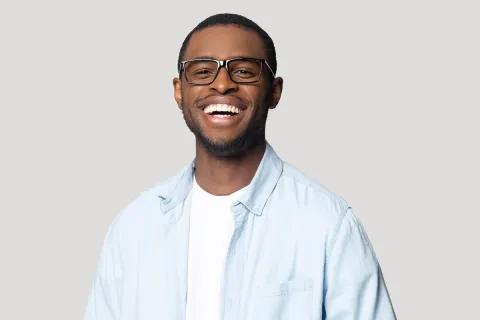 Smiling young man wearing glasses and a light blue shirt against a neutral background