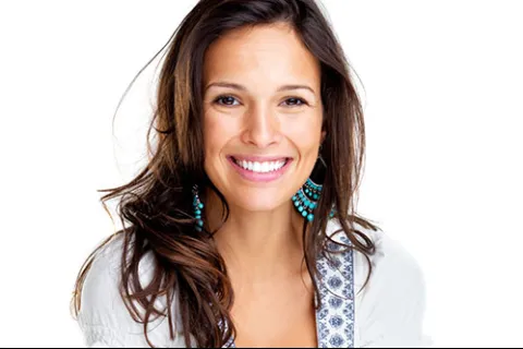 Smiling woman with long hair and blue earrings, showcasing a warm personality against a white background.