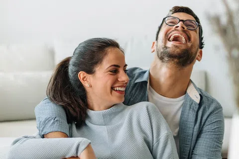 Happy couple laughing together on a couch in a bright and cozy living room.