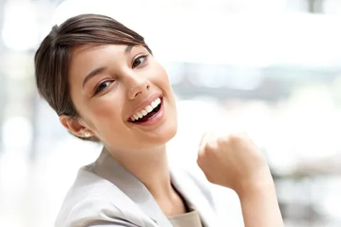 Smiling young woman with short hair and light blazer showing confidence and happiness in bright indoor setting