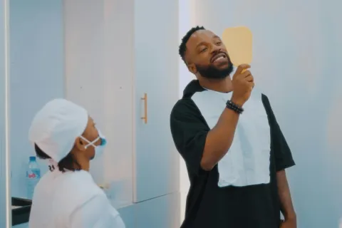 Man smiling while looking at a dental mirror held by a dentist in a clinic setting