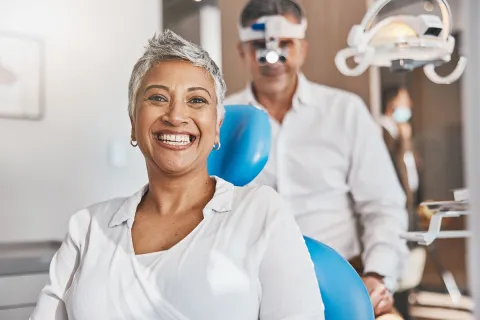 Smiling woman in dental chair with a dentist preparing for an appointment in a modern clinic.