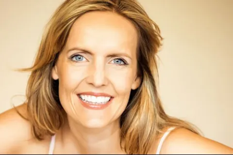 Smiling middle-aged woman with blonde hair and blue eyes against a beige background
