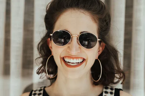 Smiling woman wearing round sunglasses and large hoop earrings with black and white checkered outfit.