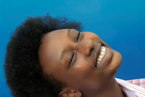 Smiling young woman with natural afro hair wearing a striped shirt against a blue background