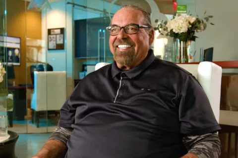 Smiling middle-aged man with glasses sitting in a modern office with flowers and glass walls.