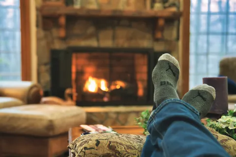 Person relaxing with feet up wearing socks in front of a cozy stone fireplace in a warm living room.