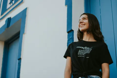 Smiling woman in casual black t-shirt stands near white building with blue door and trim outdoors.