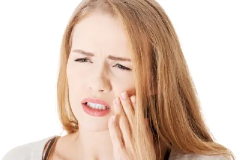 Woman experiencing dental pain, holding her cheek, with a distressed expression on her face.