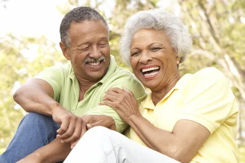 Happy older couple sitting outdoors laughing and enjoying a sunny day in casual clothes with rollerblades.