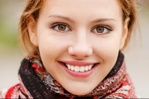 Close-up of a smiling young woman with light brown eyes and a colorful knitted scarf.