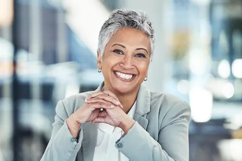 Smiling professional woman with short gray hair wearing a blazer in a modern office setting