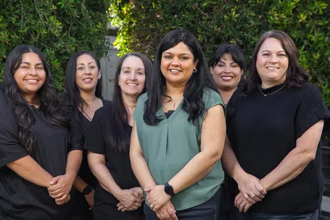 Group of six diverse women smiling outdoors with greenery background, showing unity and friendly connection