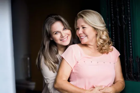 Two smiling women standing close together, showcasing warmth and affection in a well-lit setting.