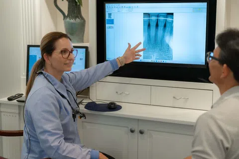 Dentist explaining a dental X-ray to a patient on a screen in a clinic setting