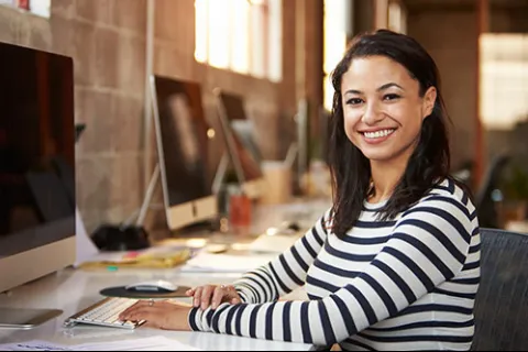 Smiling woman in striped shirt working on computer in modern bright office space
