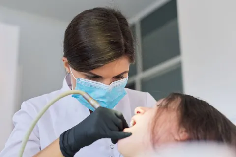 A dentist in a mask examines a patient's teeth during a dental check-up.