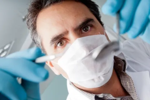 Dentist wearing gloves and mask, preparing instruments for dental examination.