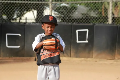 Young baseball player in Giants uniform standing on field ready to catch with glove.