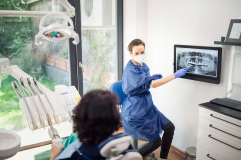 Dentist explaining X-ray to patient in a bright dental office with modern equipment.