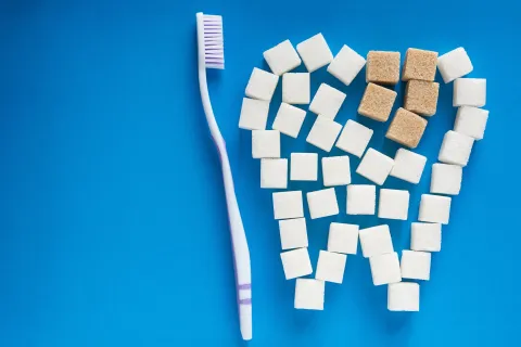A toothbrush next to sugar cubes arranged in a heart shape on a blue background.
