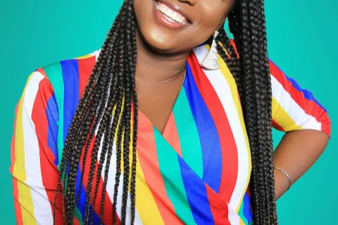 Smiling woman with long braids wearing a colorful striped dress against a teal background