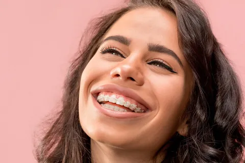 Smiling young woman with braces against a soft pink background, showcasing confidence and joy.