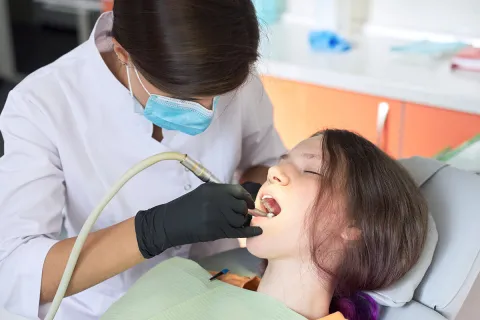 A dentist performing a dental procedure on a young girl in a clinical setting.