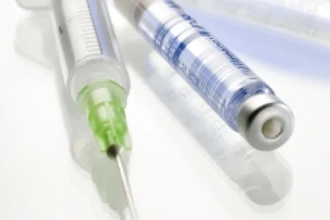 Close-up of medical syringes and needles on a reflective surface, showcasing their design and clarity.