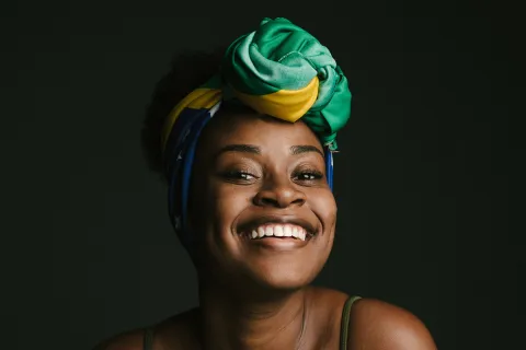 Smiling woman with a colorful headscarf against a dark background, radiating joy and confidence.