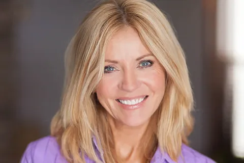 Smiling woman with blonde hair wearing a purple blouse, showcasing a warm and friendly demeanor.