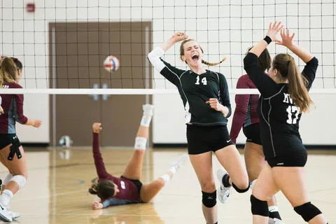 Female volleyball players celebrating a point scored during an indoor match with one player on the floor.