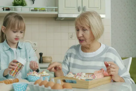 Grandmother and granddaughter decorating cupcakes together in a bright kitchen with baking ingredients on the table