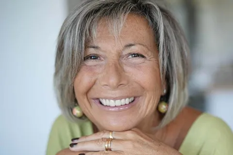 Smiling older woman with silver hair in a green top, showcasing joy and confidence indoors.