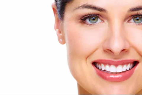 Close-up of a smiling woman with green eyes, clear skin, and white teeth on a white background