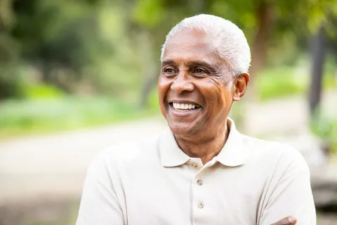 Smiling elderly man outdoors, wearing a light-colored polo shirt, embracing nature.