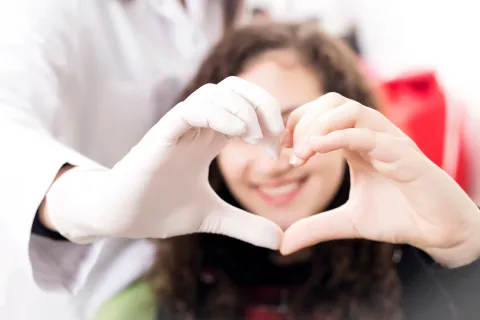 A doctor and a smiling patient form a heart shape with their hands, highlighting care and compassion.