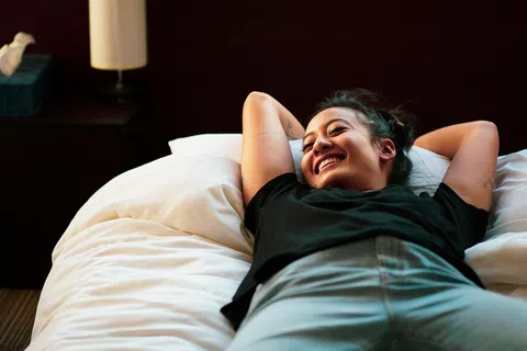 Young woman smiling and relaxing on a bed with white sheets in a cozy room.